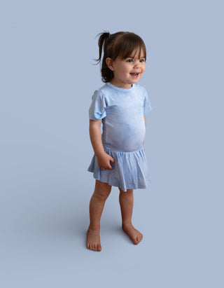 Toddler wearing light blue short-sleeve bodysuit dress with gathered skirt hem against blue background.