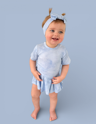 Toddler in light blue tie-dye bodysuit dress with short sleeves and flared skirt, wearing matching headband.