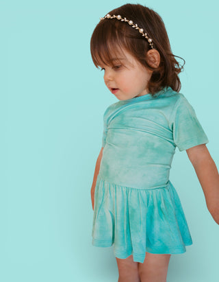Toddler wearing jade tie-dye short-sleeve bodysuit dress with gathered skirt and pearl headband.