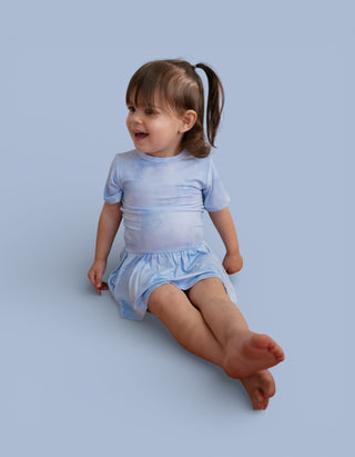 Toddler wearing light blue tie-dye short-sleeve bodysuit dress with matching skirt bottom.
