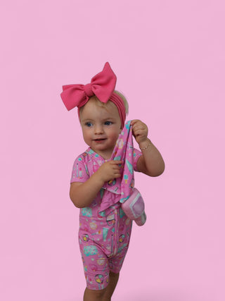 Toddler holding pink plush lovey with colorful geometric pattern against pink background.