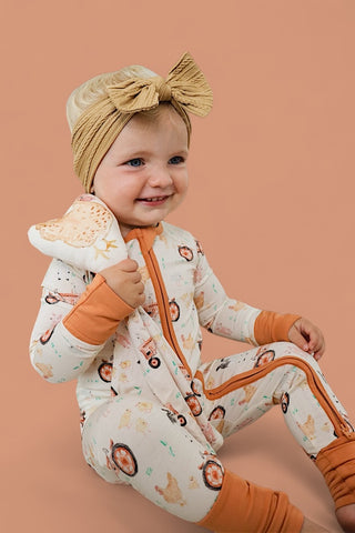 Toddler holding cream plush toy with farmyard animal print while wearing matching cream and orange pajamas with animal motifs