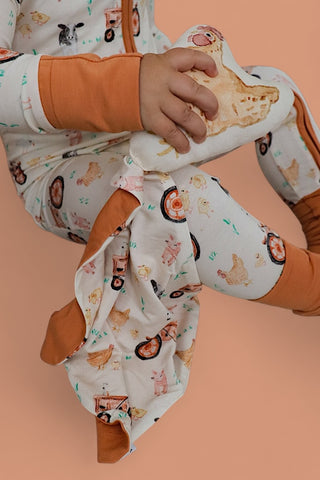 Child holding cream-colored plush toy with farmyard animal print and orange fabric accents.
