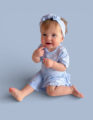 Infant wearing light blue short-sleeve bodysuit dress with matching headband.