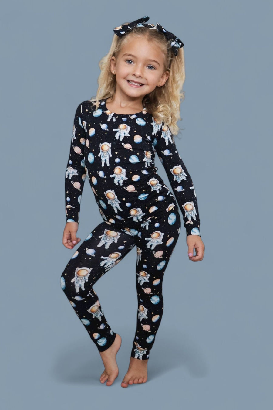 Child wearing black long-sleeve top and leggings with astronaut and planet print, paired with black hair clips.