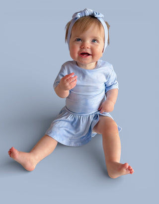Infant wearing light blue short-sleeved bodysuit dress with matching bow headband against neutral background.
