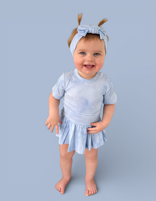 Toddler wearing light blue tie-dye bodysuit dress with short sleeves and matching headband bow.