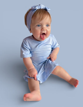 Infant wearing light blue short-sleeve bodysuit dress with matching bow headband against neutral background.