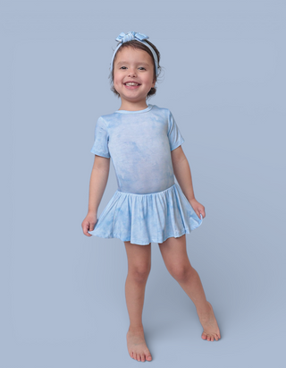 Child wearing light blue tie-dye bodysuit dress with short sleeves and skirt, paired with matching hair bow.
