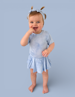 Toddler wearing light blue tie-dye bodysuit dress with short sleeves and flared skirt against blue background.
